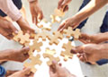 Many hands hold puzzle pieces and collaborate to put them together