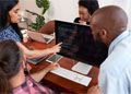 Four people sit around a desk, looking at information on a laptop