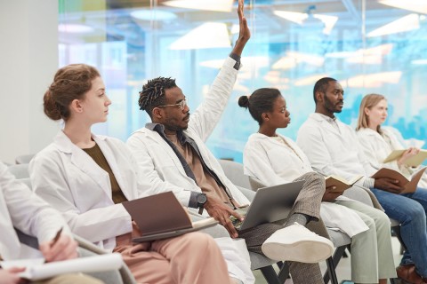 Medical students in a class, one with a hand raised.
