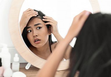 woman looks at her hair in mirror