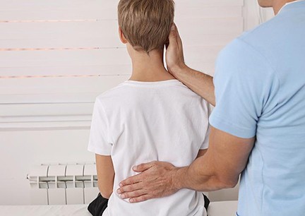 photo of young person's back and healthcare provider checking the spine