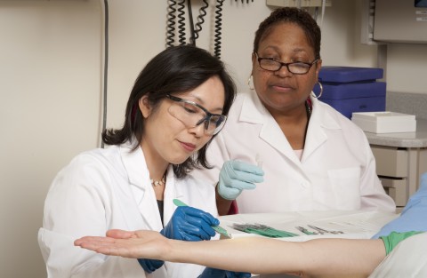 NIAMS IRP senior investigator Dr. Heidi Kong performs a non-invasive collection of skin samples with the assistance of Sheila Phang, a research nurse