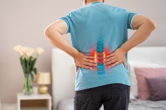 Photo of the back of a man with his hands on his lower back, depicting a patient with lower back pain.