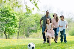 Family of four people playing soccer outside
