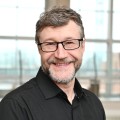 Headshot of a man with curly hair and glasses.