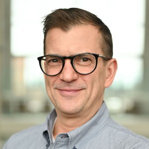 Headshot of a man in a dress shirt with short hair, wearing glasses.