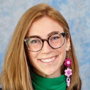 Photo of a woman with long red hair and glasses, smiling.