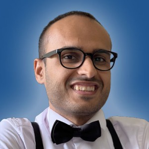 Headshot of a young man, with very short hair, wearing glasses, a shirt and bow tie. He is smiling.