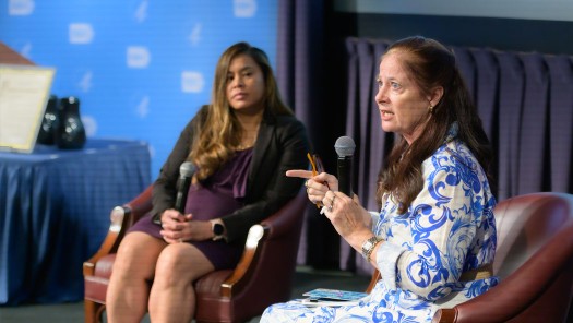 A woman with a microphone, with another woman blurred in the background