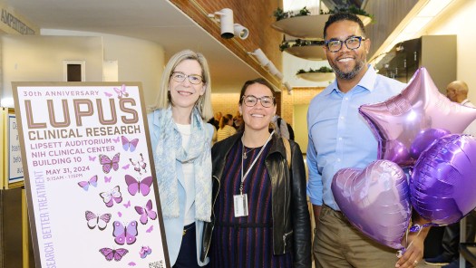 Three people smiling next to a Lupus poster.