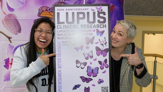 Two woman smiing, holding a Lupus poster.