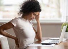 Distressed woman holds her head and her back because her back hurts