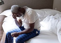 Photo of man sitting on bed with his head in his hands